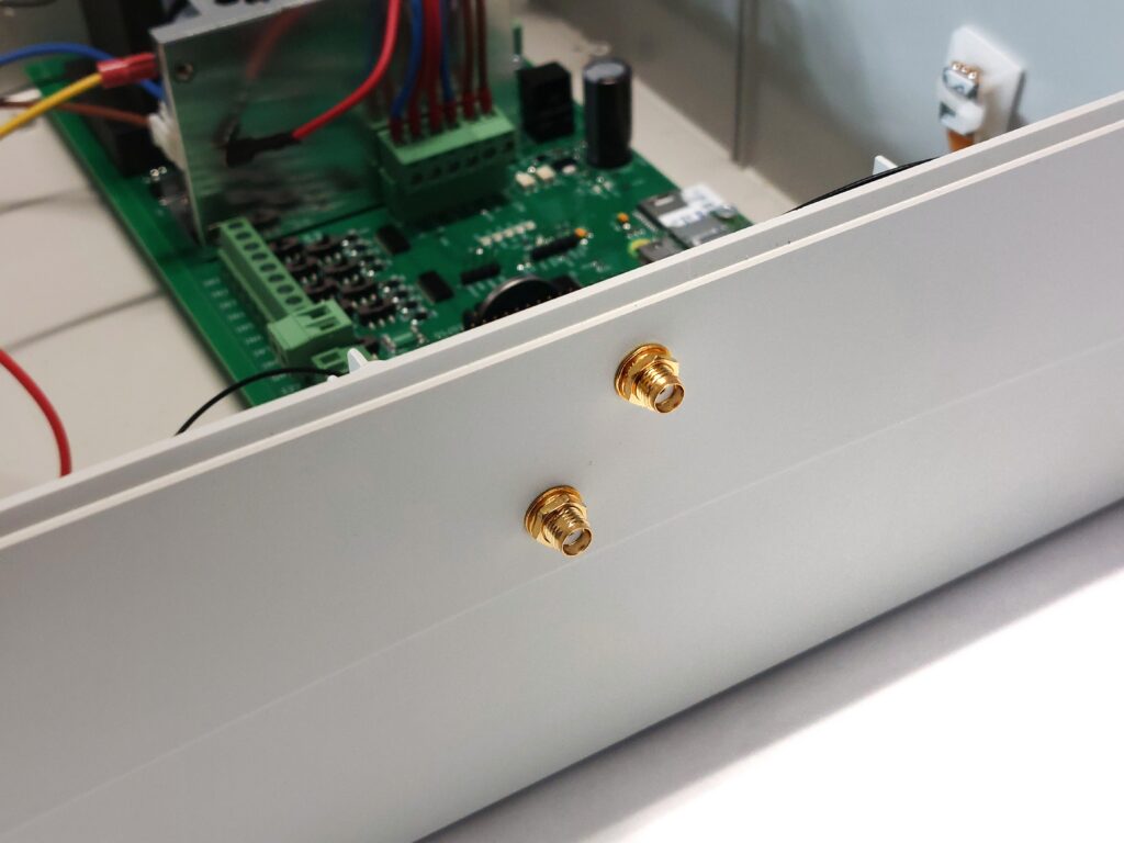 A close-up of the outer side panel of the plastic enclosure. Two empty, protruding gold-colored antenna sockets are visible; the antennas should be screwed into these sockets. This photo shows the "before" condition, before the antennas are screwed in.