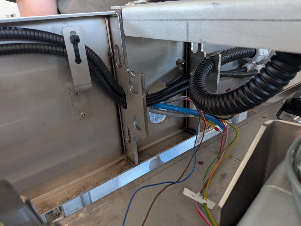 Widok przewodów elektrycznych i peszla przeprowadzonych przez metalowy wspornik montażowy słupka od wewnętrznej strony klatki.