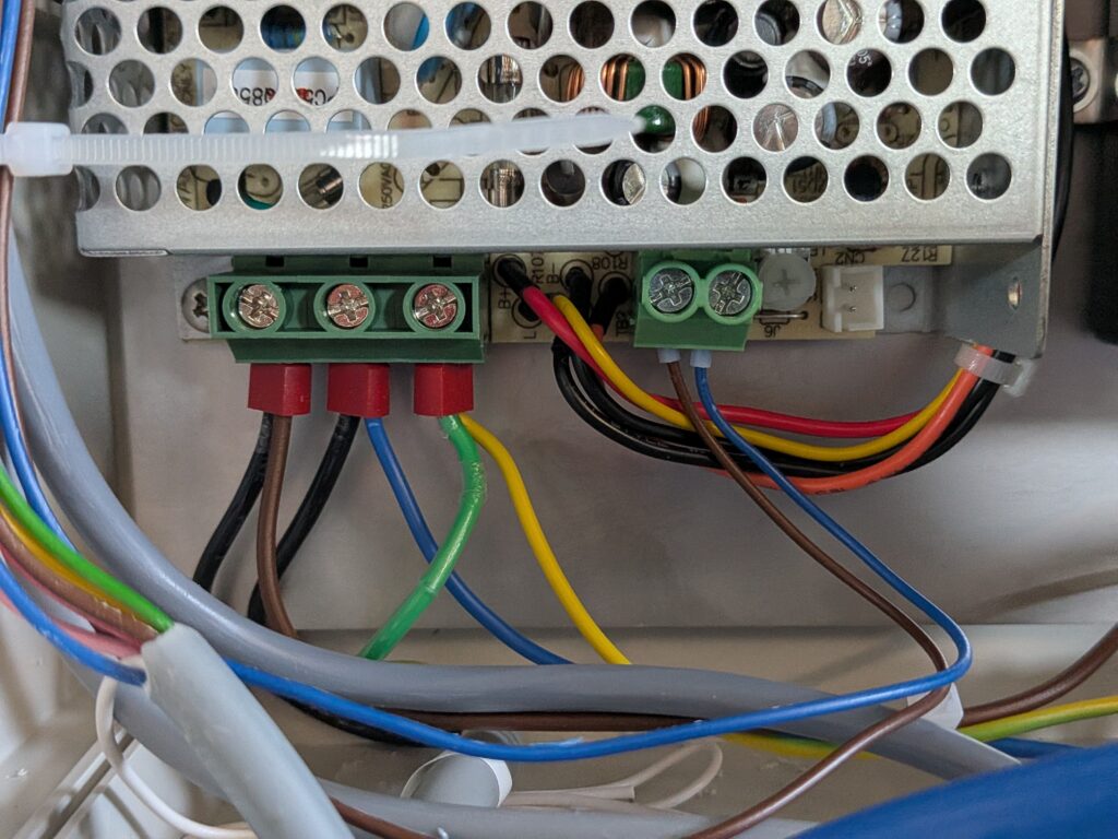 Zbliżenie na zaciski zasilacza sterownika z podłączonymi przewodami fazowym, neutralnym i ochronnym.